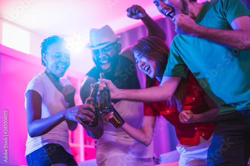 Group of people enjoy night glow disco party singing songs, dancing, drinking alcohol at private home by blue and pink light