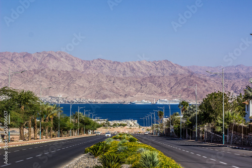 south Middle East city view park outdoor district car road down to Gulf of Aqaba Red sea bay, palm trees alley way, bare desert mountain ridge horizon background in Jordan Arabian country 