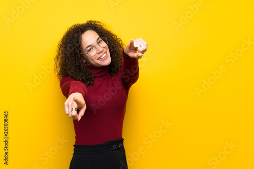 Dominican woman with turtleneck sweater points finger at you while smiling