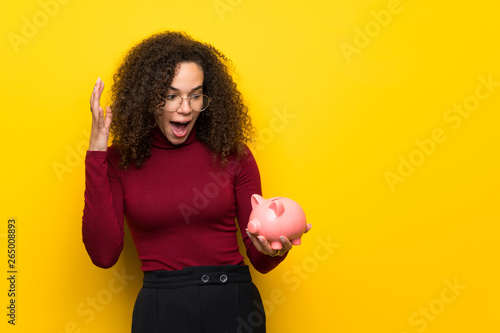 Dominican woman with turtleneck sweater surprised while holding a piggybank