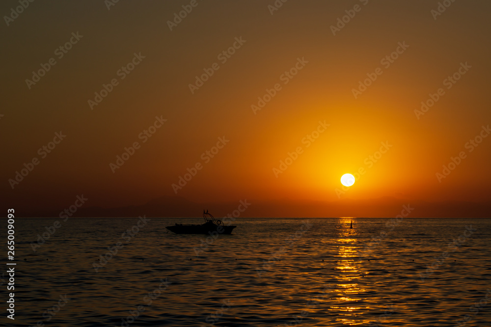 Orange summer sunset on sea with rocks and boat