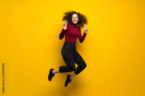 Dominican woman with curly hair jumping over isolated yellow wall