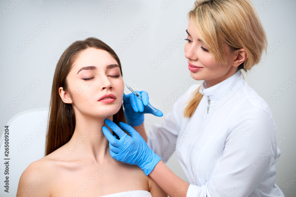 Beautician doctor with botulinum toxin syringe making injection to to remove crow's feet. Cheek volume enhance mesotherapy. Anti-aging treatment and face lift in cosmetology clinic. Beautician doctor with botulinum toxin syringe making injection to to remove crow's feet. Cheek volume enhance mesotherapy. Anti-aging treatment and face lift in cosmetology clinic.