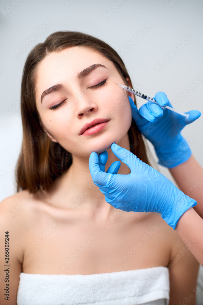 Beautician doctor with botulinum toxin syringe making injection to to remove crow's feet. Cheek volume enhance mesotherapy. Anti-aging treatment and face lift in cosmetology clinic. Beautician doctor with botulinum toxin syringe making injection to to remove crow's feet. Cheek volume enhance mesotherapy. Anti-aging treatment and face lift in cosmetology clinic.