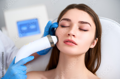 Canvas Print Beautician doctor doing rf-lifting procedure for flawless woman face laying in a beauty salon
