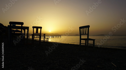 Empty wooden chairs on pebble beach during dramatic sunset. Summer is coming and outdoor / outside conceptual photo. Amazing sunset over mountains & ocean horizon at weekend. Sunny day at outdoor cafe © Akin Ozcan