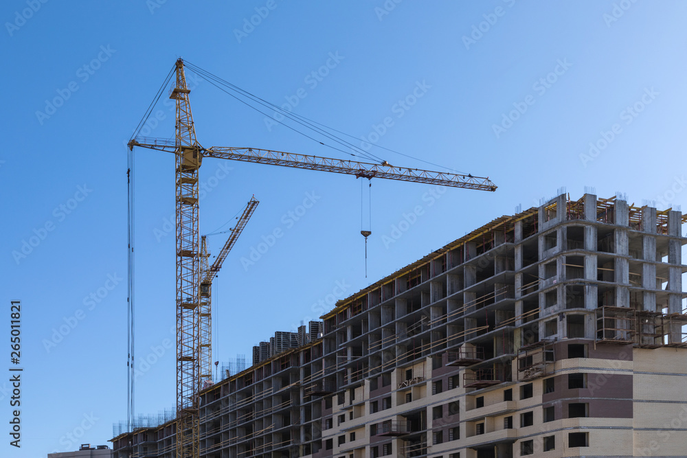 The building of the house. The crane and the new brick building in the clear sunny day on the background of blue sky The building of the house. The crane and the new brick building in the clear sunny day on the background of blue sky