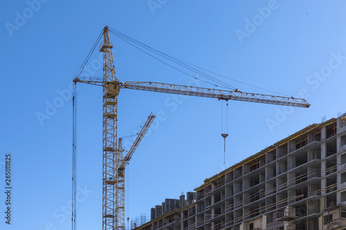 The building of the house. The crane and the new brick building in the clear sunny day on the background of blue sky