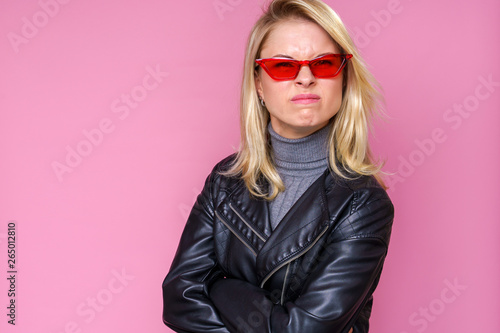 Image of serious blonde woman in pink glasses and leather jacketisolated on pink background