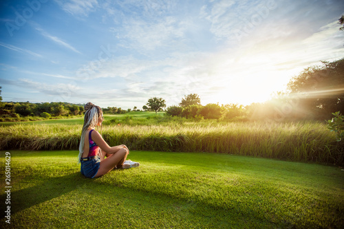 Girl with African braids sitting on the lawn and watching the sunset. copy space