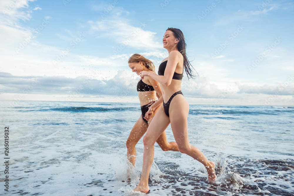 Two girls girlfriend in black swimsuits play sports, run on the beach.
