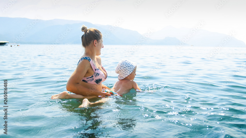 Beautiful young woman teaching her little child swimming in th elake