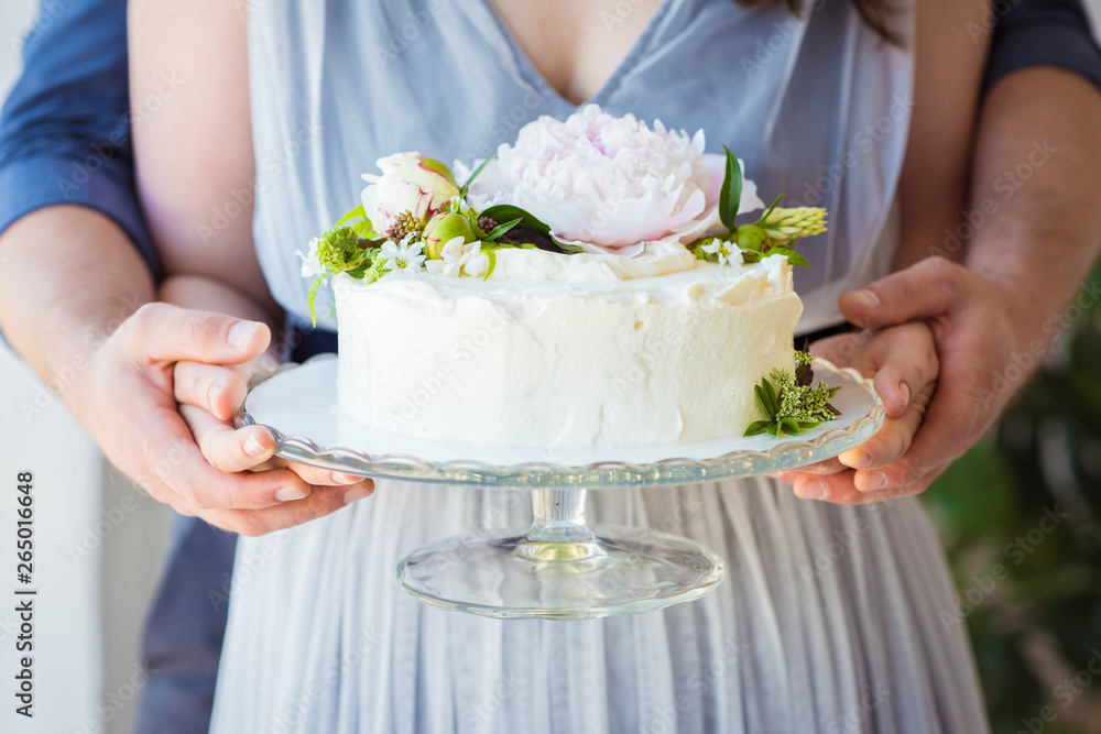 Woman holding birthday Cake decorate with flowers on a glass stand. Celebration concept. Trendy layer cake Woman holding birthday Cake decorate with flowers on a glass stand. Celebration concept. Trendy layer cake