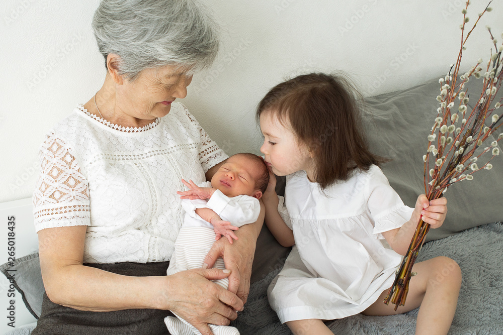 Greatgrandmother hugs two greatgranddaughters. Grandmother sits with