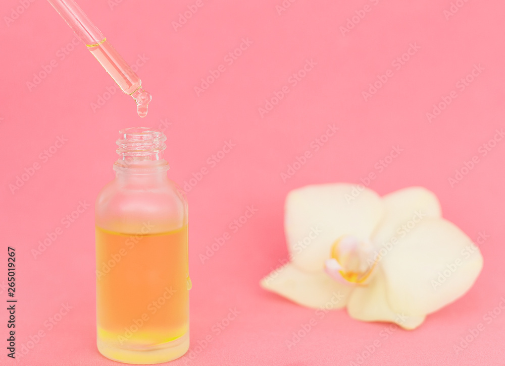 Oily drop falls from a cosmetic pipette, flower. pink background, space for text. Pipette with essential liquid, closeup