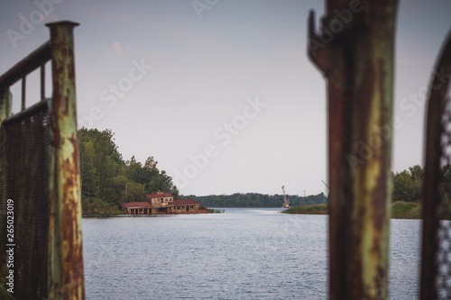 Curve fence on the old pier in Pripyat near the water. Abandoned radioactive city. Destroyed ship on the river.
