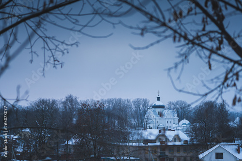 Church in the winter. Temple under the snow. Monastery with a black dome in the village. Vignetting black branches of trees. photo