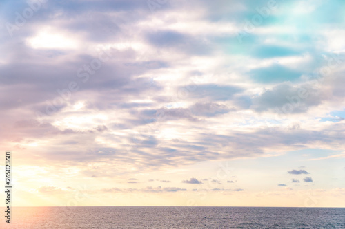 Impressive white and pink clouds on blue sky over calm sea with sunlight reflection.