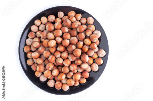 hazelnuts: many nuts lie on a black plate, on a white background, top view