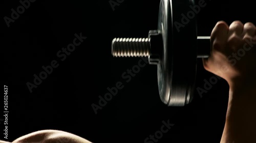 Man building muscles close up. Detail of young bodybuilder lifting weight on dark background. Lifting dumbbells for bigger biceps. photo