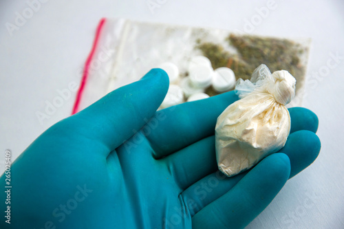 synthetic drugs: a laboratory technician holds in his hand a package of opiate powder against the background of samples of narcotic preparations of plant origin