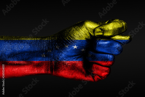 A hand with a painted Venezuela flag shows a fig, a sign of aggression, disagreement, a dispute on a dark background.