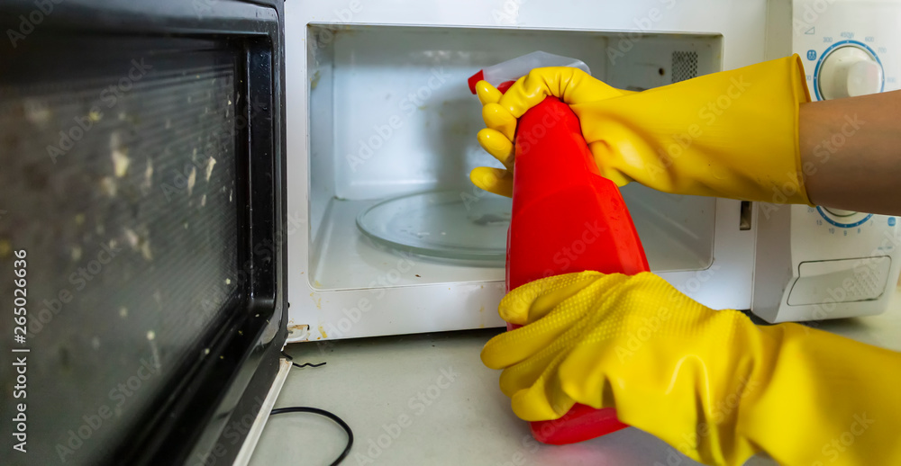Woman hands in rubber gloves washing microwave