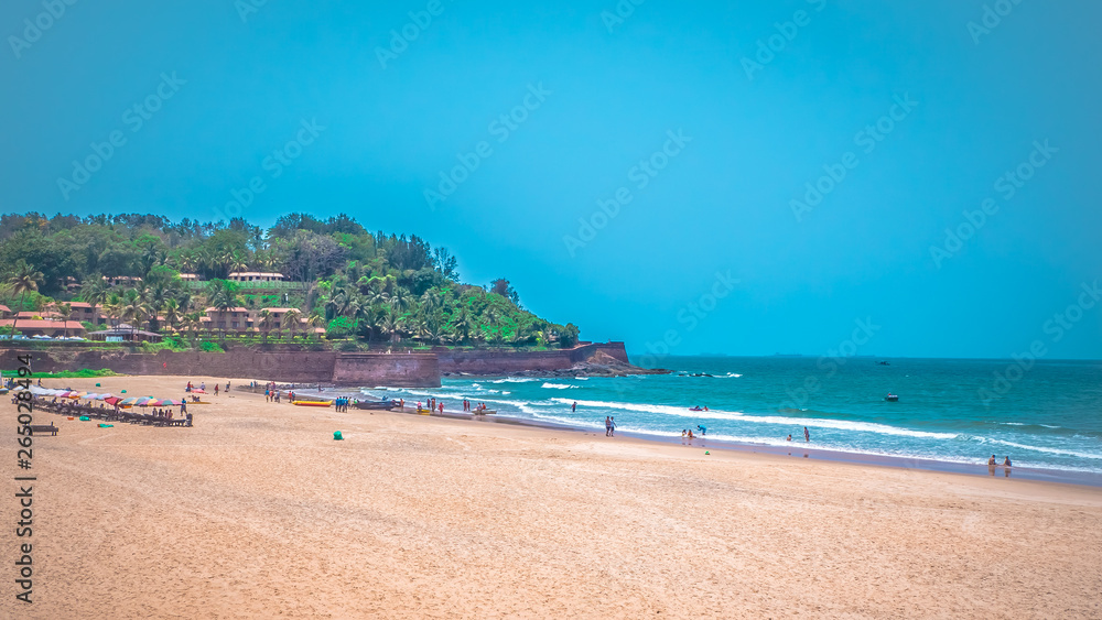 North Goa, India Candolim beach with Aguada fort in the background. Famous tourist summer vacations destination on the beach by Arabian Sea in Goa tropical climate with coconut palms.