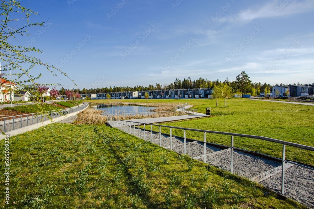 Amazing view of suburbian landscape. Path to little pond and cute compact suburbian houses on blue sky background. Sweden. Europe.