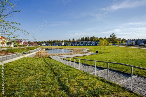Amazing view of suburbian landscape. Path to little pond and cute compact suburbian houses on blue sky background. Sweden. Europe. © Alex