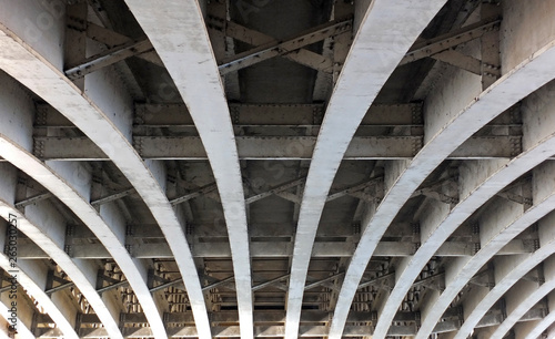 perspective view of curved arch shaped steel girders under an old road bridge with rivets and struts painted grey