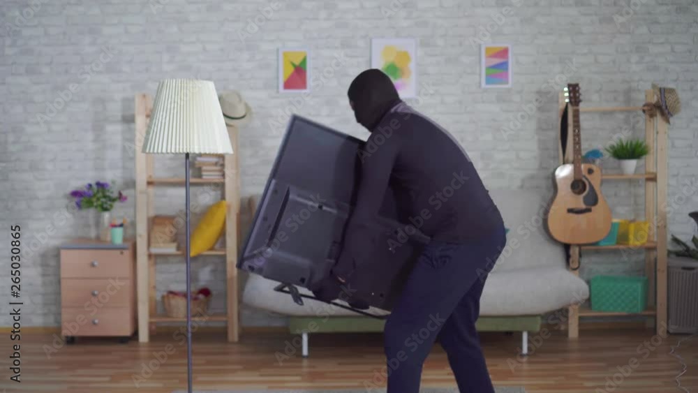 anonymous thief in a Balaclava mask stealing TV in the house and experiencing back pain injury anonymous thief in a Balaclava mask stealing TV in the house and experiencing back pain injury