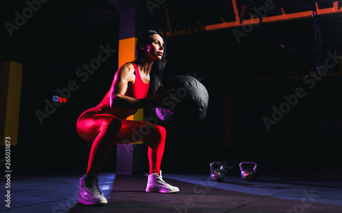Sportswoman doing squat exercises with fitness ball. Female exercising and stretching with medicine ball at gym.