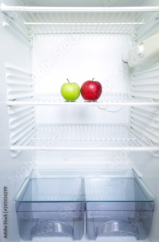 Bright fresh red and green apples on shelf of open empty refrigerator. Weight loss diet concept.