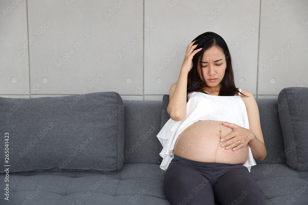 pregnant woman is sitting in living room and stressed another hand holding her stomach pregnant woman is sitting in living room and stressed another hand holding her stomach