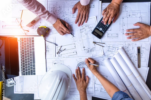 engineers pointing to building on blueprint and using laptop to drawing design building Project in office, construction concept. Engineer concept