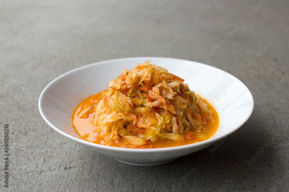 Stir fried cabbage and tomatoes in a white bowl against grey cement background. Stir fried cabbage and tomatoes in a white bowl against grey cement background.