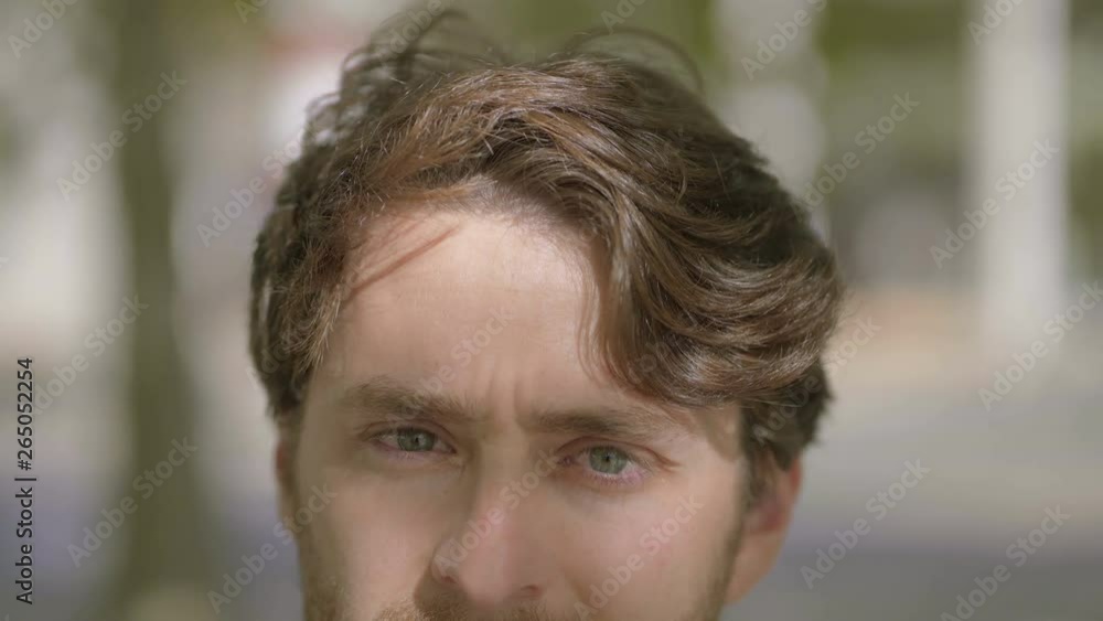 Handsome man looking at camera outdoor. Half face portrait of handsome brunette man looking at camera at sunny day, handheld shot. Facial expression concept Handsome man looking at camera outdoor. Half face portrait of handsome brunette man looking at camera at sunny day, handheld shot. Facial expression concept