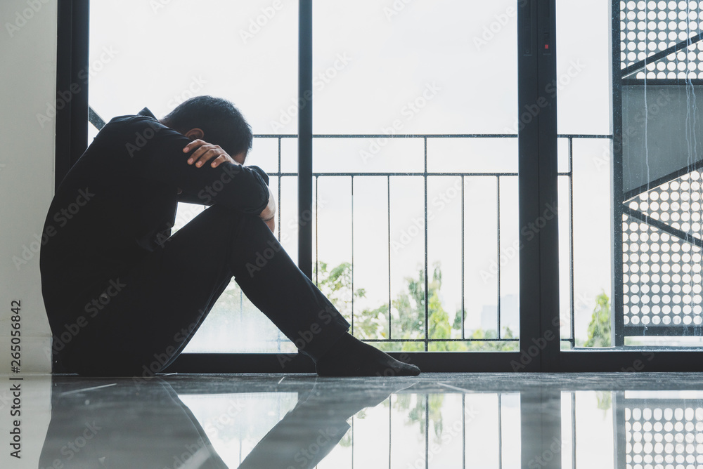 Fototapeta premium Depressed man sitting on floor near window at home feeling lonely dramatic and sad.