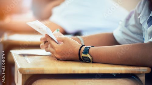 Hand of students writing and taking exam with stress in classroom