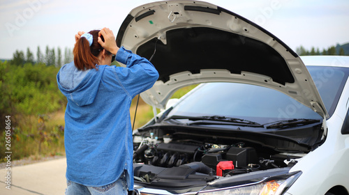Young woman feel stress and standing in front of a broken down car open engine compartment hood on the road.