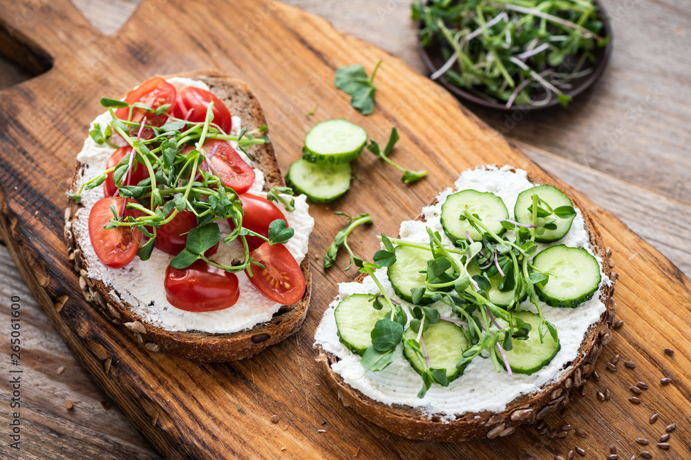 Healthy toasts with cream cheese, cucumber, cherry tomato and microgreen on wooden board. Appetizer or breakfast food