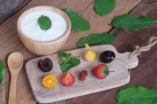 Natural homemade plain organic yogurt mixed with fresh berry fruit white bowl and wood spoon on wood texture background