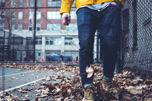 Close-up of man's legs wearing jeans and yellow raincoat walking among fallen leaves