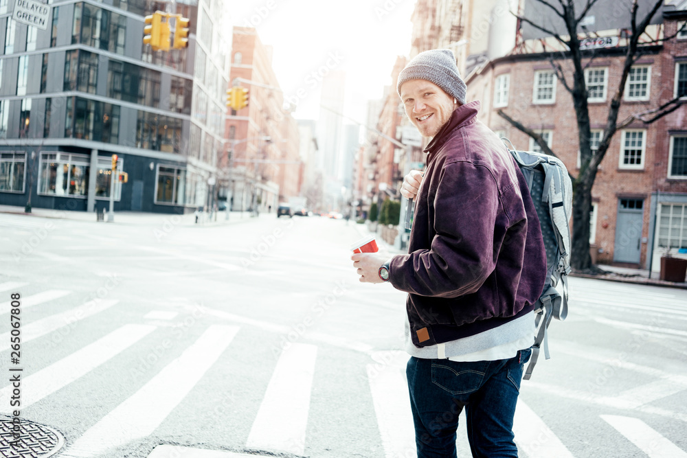 Young casual man crossing city street with cup of coffee in hand