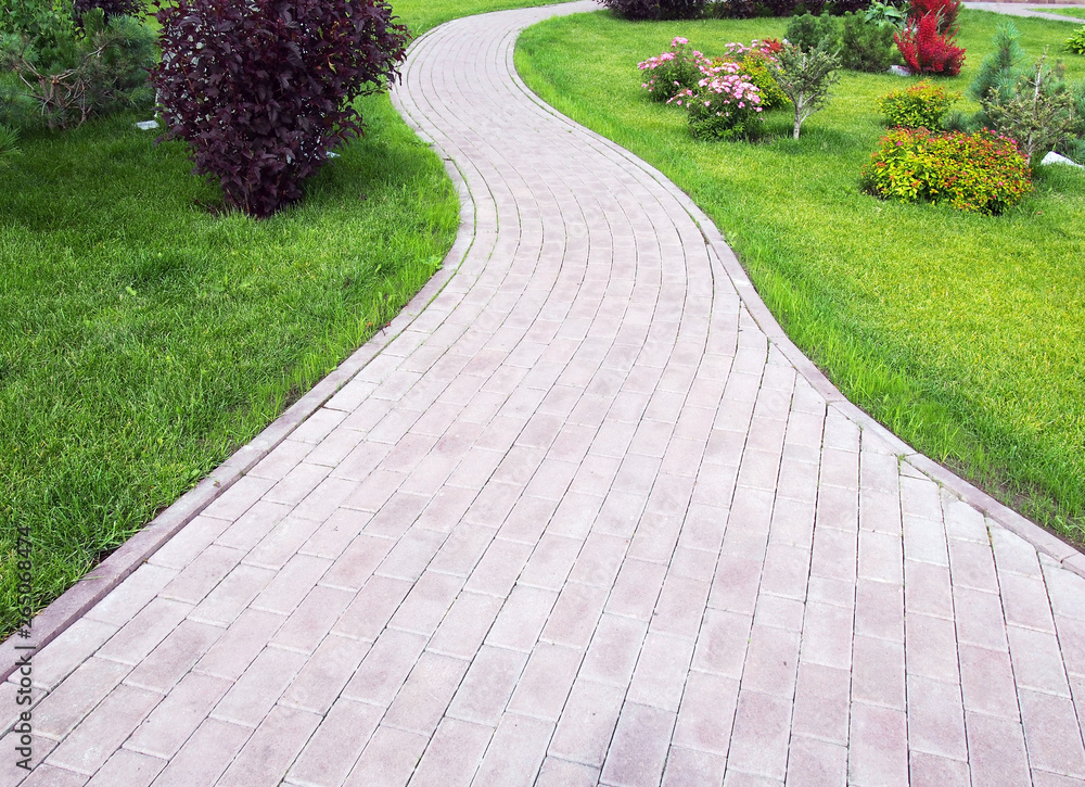Obraz premium Curved footpath paved with bricks running ahead along a green grassy lawn. Landscaping design