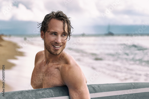 Sexy surfer surfing man with surfboard. Handsome young male athlete holding surf board with wet hair on summer beach sport holiday. Sports travel destination. Surfing lifestyle.