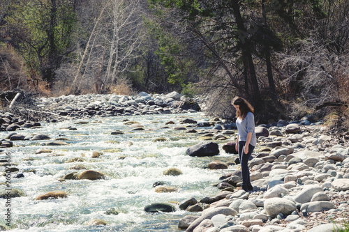 Young beautiful girl on nature by the river. Good mood on a bright spring day. Against the background of the forest and a beautiful mountain river. Tourism and travel.