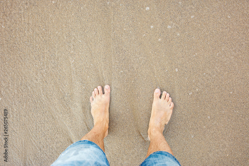 Man's feet on the sand on coastline.