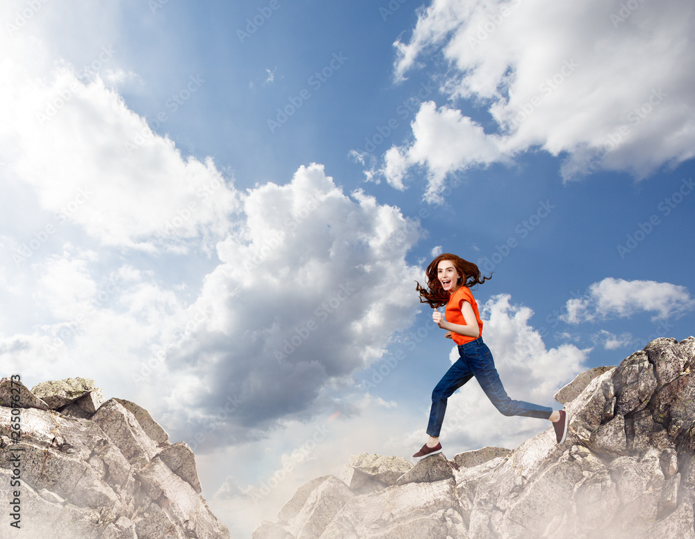 Redhead woman jumps over cliff on blue sky background.